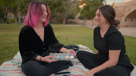 two women laughing and playing with face paint in a park