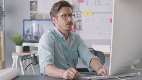 arquitecto masculino discapacitado en silla de ruedas en la oficina trabajando en una computadora de escritorio usando una tableta gráfica