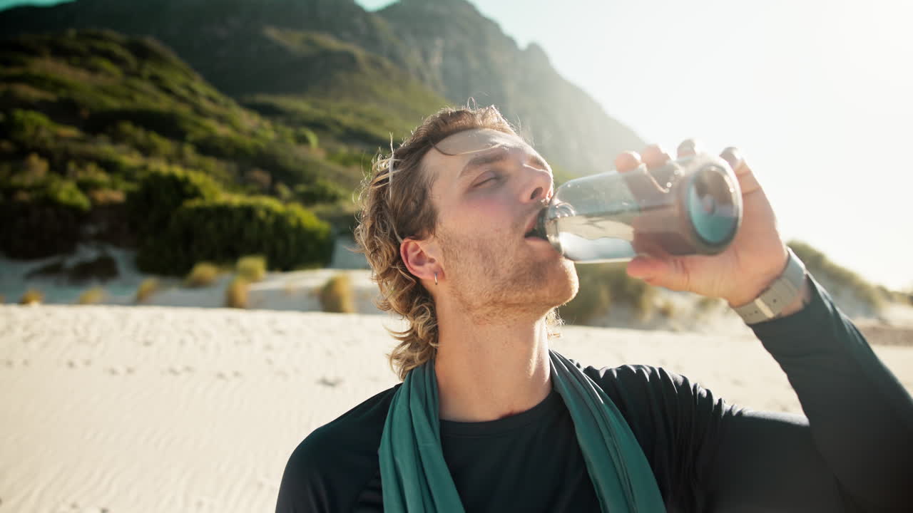 Junger Mann trinkt Wasser an einem sonnigen Strand