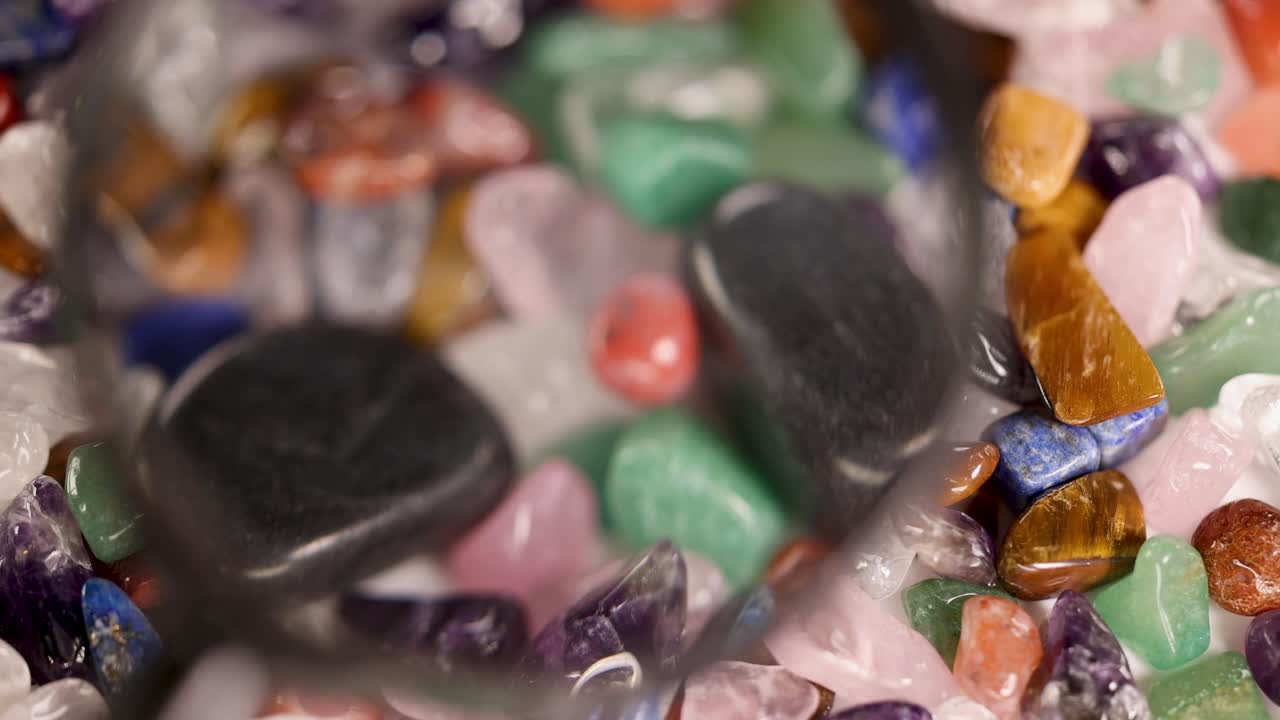 A magnifying glass highlights colorful chakra stones, enhancing their textures and hues under bright lighting