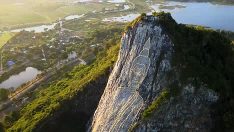 4k top down aerial pan above carved buddha image made from gold on a cliff at khao chee chan, pattaya, thailand