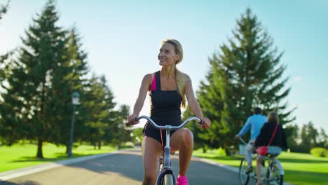 happy woman enjoying bicycle ride and waving hand in summer park. riding bicycle