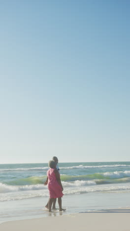vertical video of senior african american couple walking at beach, in slow motion
