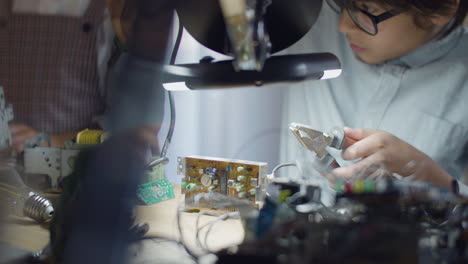 smart boy in glasses using iron and pliers for welding wires