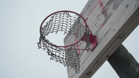 Old-basketball-hoop-with-torn-net-hanging-in-wind-and-peeled-off-paint