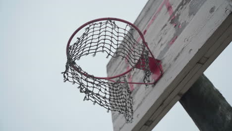 old basketball hoop with torn net hanging in wind and peeled off paint