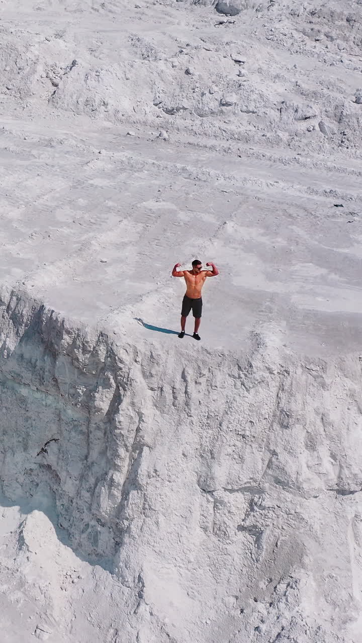 Shirtless sportsman on the rocky canyon. Aerial view of a strong man posing on the top of the hill in summer. Natural mountainous background. Vertical video