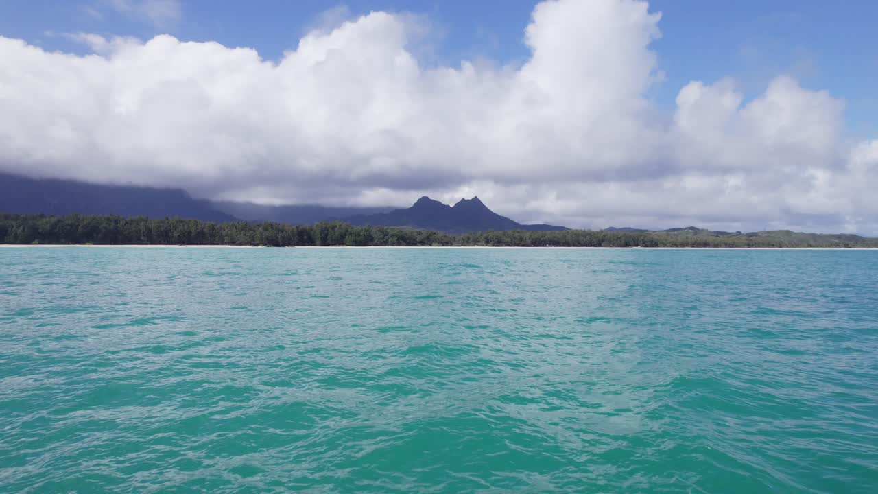 A serene view from the water looking toward the Windward coast of Oʻahu, where turquoise ocean meets rainforest and mist-covered mountains.