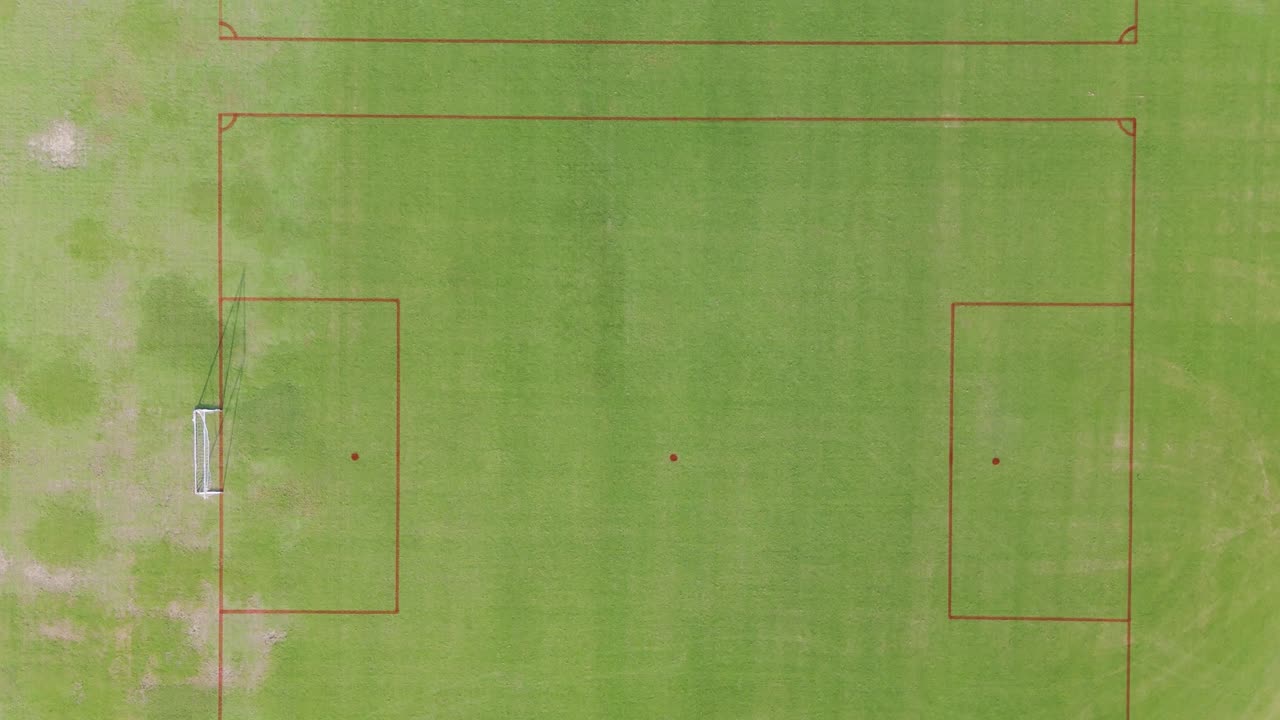 Drone footage captures an empty soccer field from above, showcasing its layout and surroundings in bright daylight
