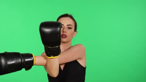 joven y hermosa mujer morena caucásica con guantes de boxeo y mirando hacia la cámara estira los brazos con pantalla verde en el fondo