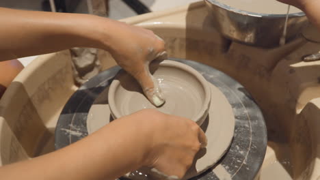 woman's hands shaping mound of clay making bowl on potter wheel during pottery workshop