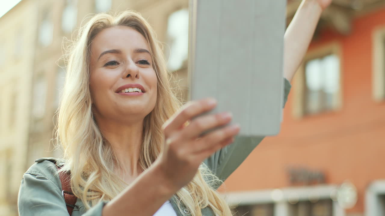 Close-up view of blonde young woman making a video call on the tablet and walking down the street