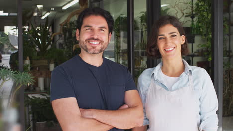 portrait of male and female owners of florists standing in doorway surrounded by plants