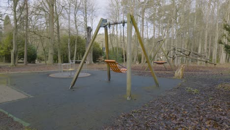 children's empty playground single orange swing chair rocking alone in woodland autumn forest