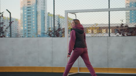 gym enthusiast jogging round sports court in urban environment surrounded by modern tall buildings under clear sky maintaining energetic stride focused on routine before sunset warm glow