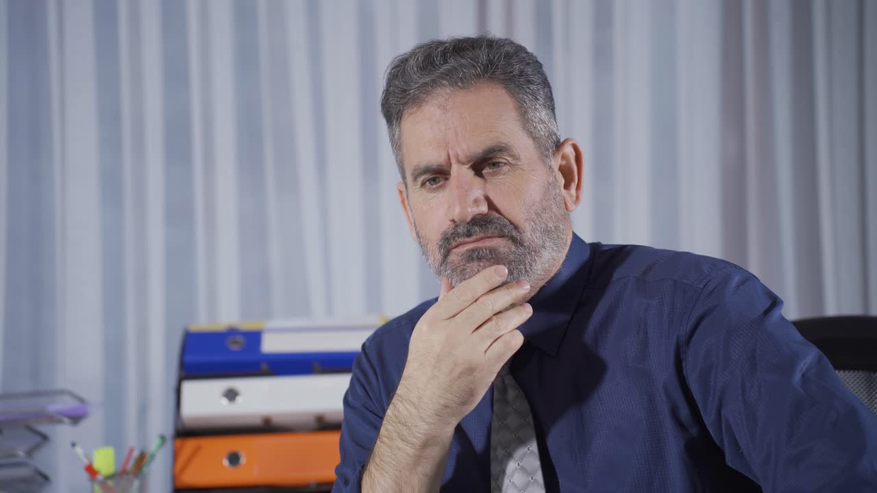 hombre de negocios maduro reflexivo mirando a la cámara, jugando con la barba, pensando en una idea.