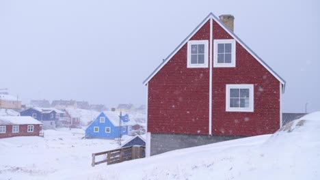 red house in a snowstorm with other houses behind in ilulissat, greenland