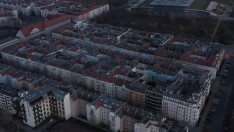 Aerial-slow-motion-view-of-traditional-brick-house-rooftop-across-street-and-lane-surrounded-with-trees-on-a-cloudy-early-morning-in-Berlin,-Germany