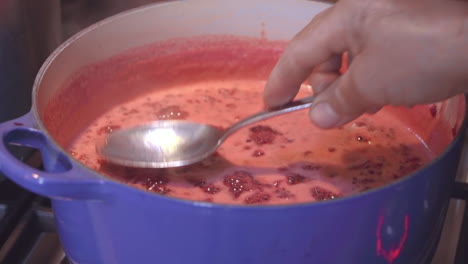 raspberry puree bubbling in pot while man checks consistency with spoon, close up