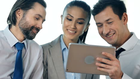 A-Work-Team-Consisting-Of-Two-Men-And-A-Woman-Make-A-Videocall-With-A-Tablet