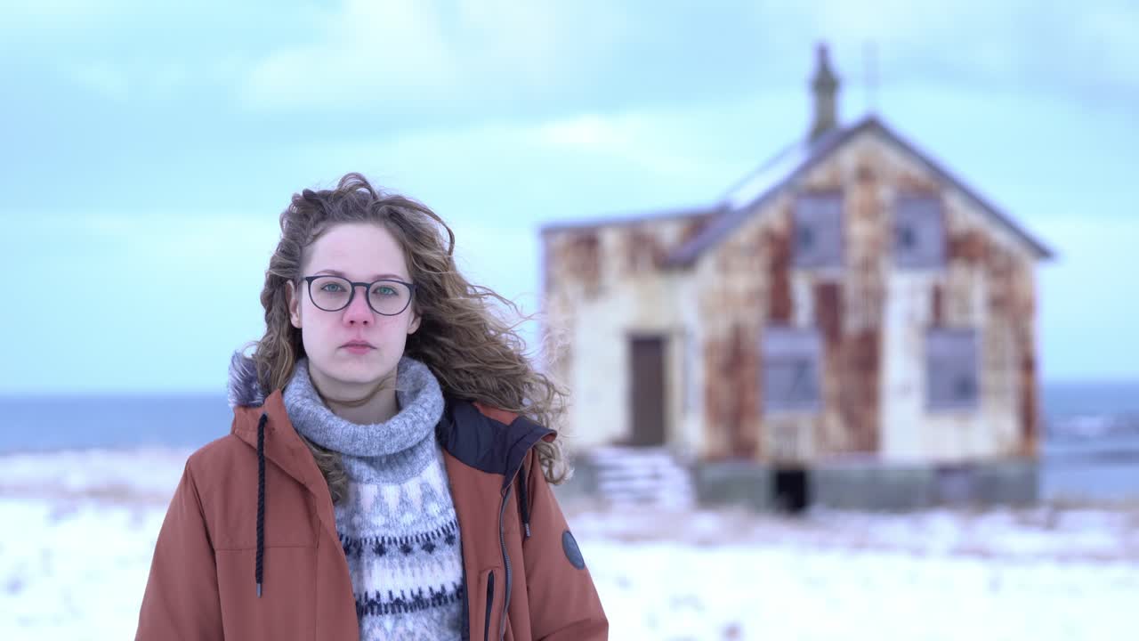 Camera focuses between young girl and abandoned, rusty house. Stable shot showing a portrait at 90mm view.