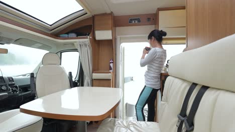 mujer en el interior de una autocaravana con una taza de café mirando la naturaleza.