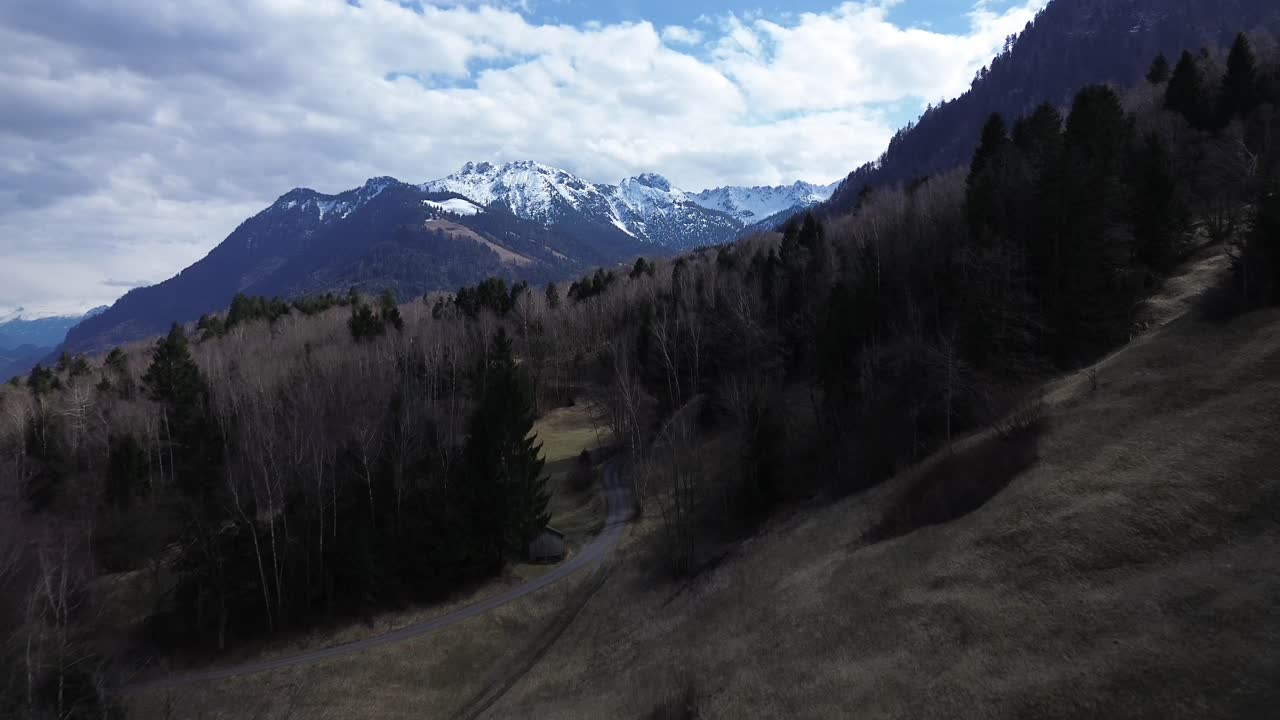 Drone fly above Forest with Mountain Road with Snow Covered Summits in Background. Austria, Europe