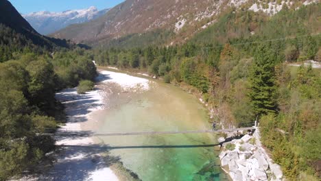 drone inclinado hacia arriba, hombre caminando a través del puente de cuerda sobre el hermoso río alpino cristalino