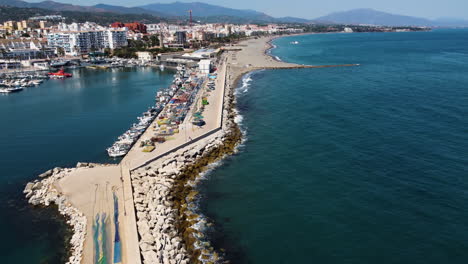 A-drone-tilts-over-the-crowded-beach-waterfront-of-Estepona,-Spain