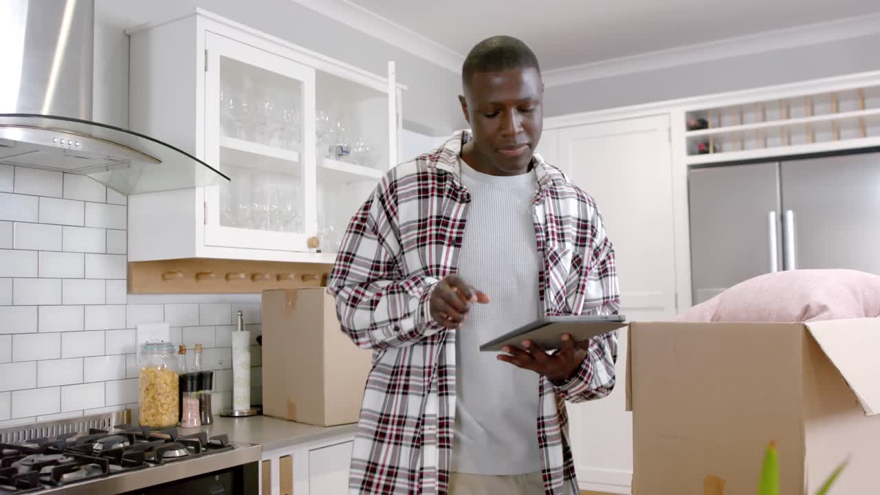 African american man unpacking boxes and using tablet in kitchen at home, slow motion