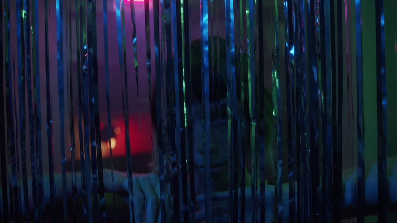 A young woman stares int the camera through glittering curtain