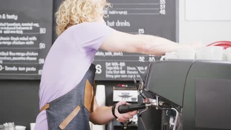 Caucasian-male-barista-wearing-apron-preparing-coffee-with-coffee-machine-in-cafe