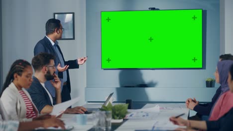 reunión en la sala de conferencias de una oficina multiétnica: un ingeniero industrial indio utiliza la televisión para presentar el concepto de motor de energía verde a un equipo de técnicos.