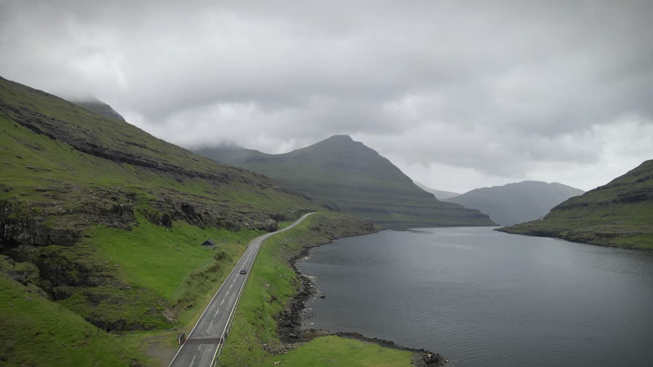 파로 섬의 풍경적인 해안 도로, 푸른 풍경과 험난한 절벽을 가로질러 바람이 불고, 조용한 물과 흐린 하늘 아래의 극적인 봉우리, 평화롭고 멀리 떨어진 전망을 제공합니다.