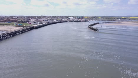 aerial-view-rising-up-from-river-level-towards-the-harbour-at-Amble-in-Northumberland-UK,-from-the-river-mouth