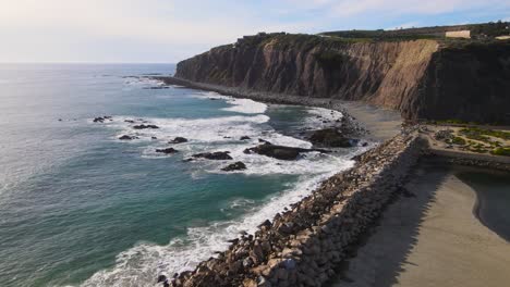 aerial dolly over rock wall, ocean waves crash in front of majestic sea cliff