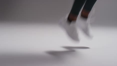 close up shot showing feet of female athlete wearing tracksuit and training shoes in gym fitness class running on the spot against plain background in real time