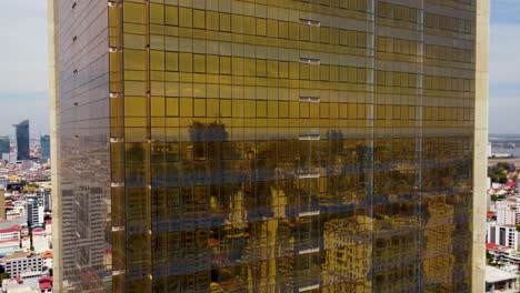 phnom penh city highrise buildings reflected in golden facade of a modern skyscraper, gold tower 42 glass facade, drone shot, closeup view