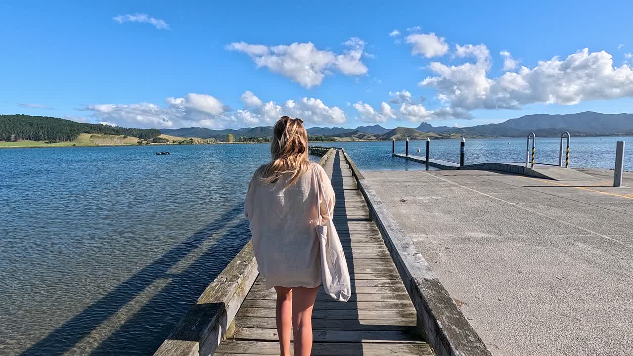 Una donna cammina lungo il molo del Matarangi Freedom Camp nell'Isola del Nord della Nuova Zelanda. Le acque calme e i paesaggi pittoreschi creano un'atmosfera tranquilla e rilassante in riva al lago