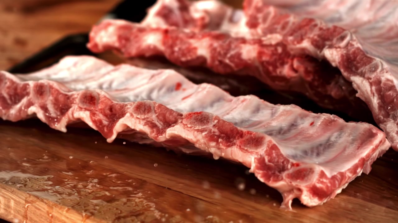 Fresh Raw Pork Ribs Dropping onto a Wooden Cutting Board