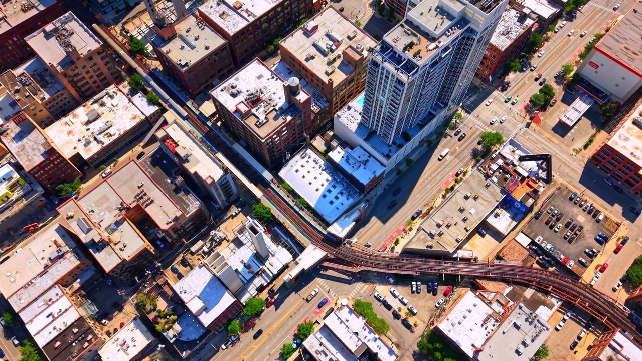Grade densa de telhados com linha de trem elevada, Chicago. Vista aérea de drone revela uma ferrovia elevada sinuosa serpenteando entre telhados de armazéns, estacionamentos e ruas da cidade.
