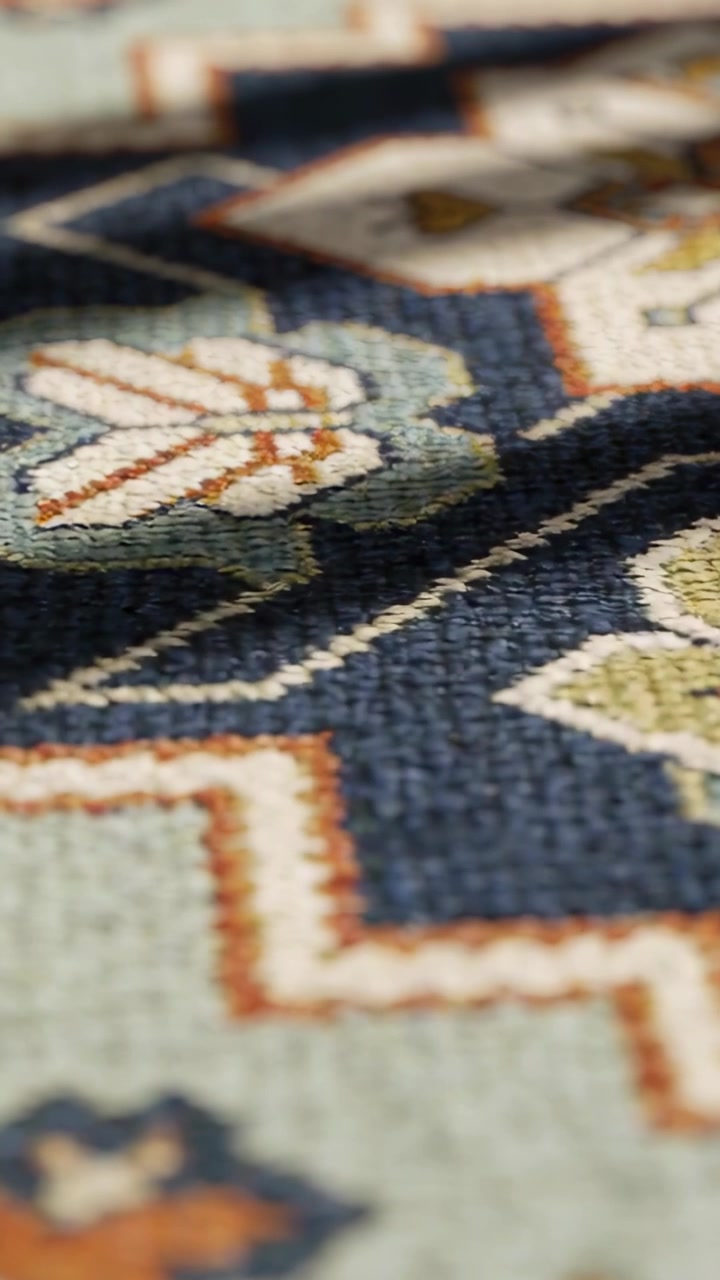 Vertical video: Shifting camera revealing woven patterned rug on floor, showing thread texture