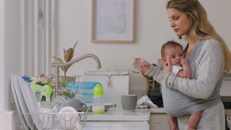 madre hermosa sosteniendo a su bebé trabajando en casa lavando platos limpiando la cocina cuidando al niño haciendo tareas domésticas disfrutando de la maternidad