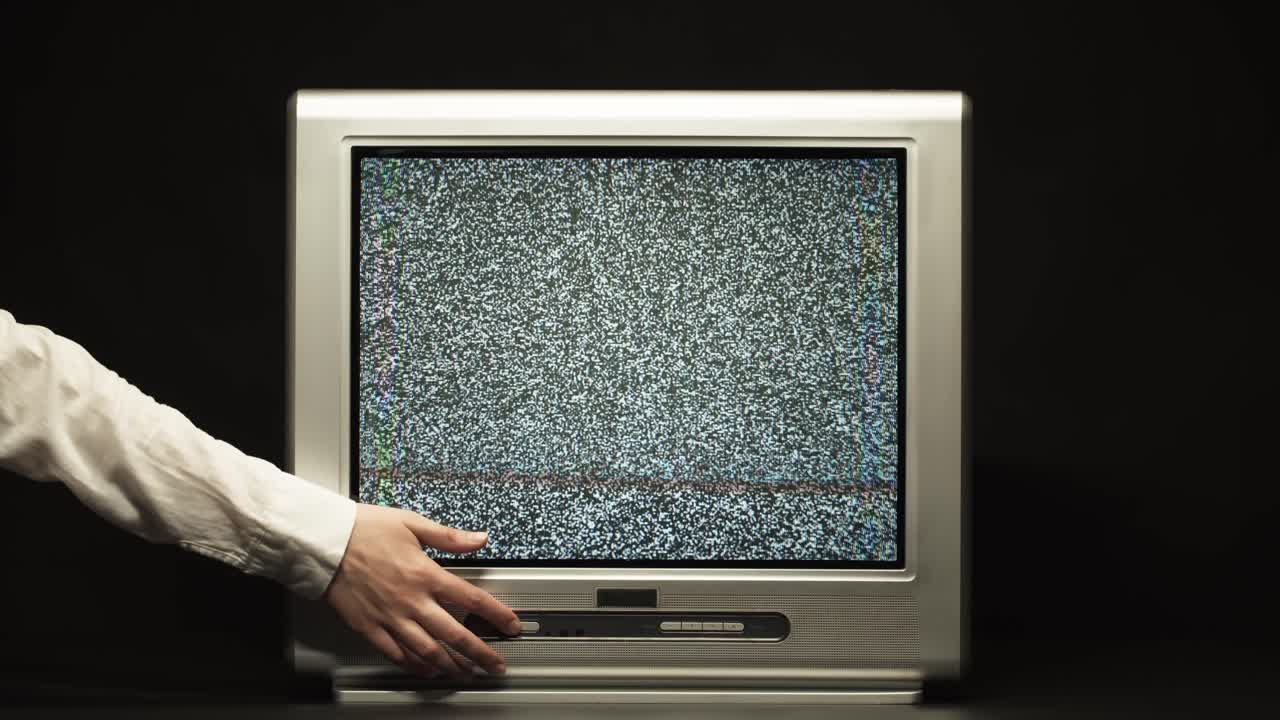 Mano che spegne una vecchia televisione CRT con effetto neve