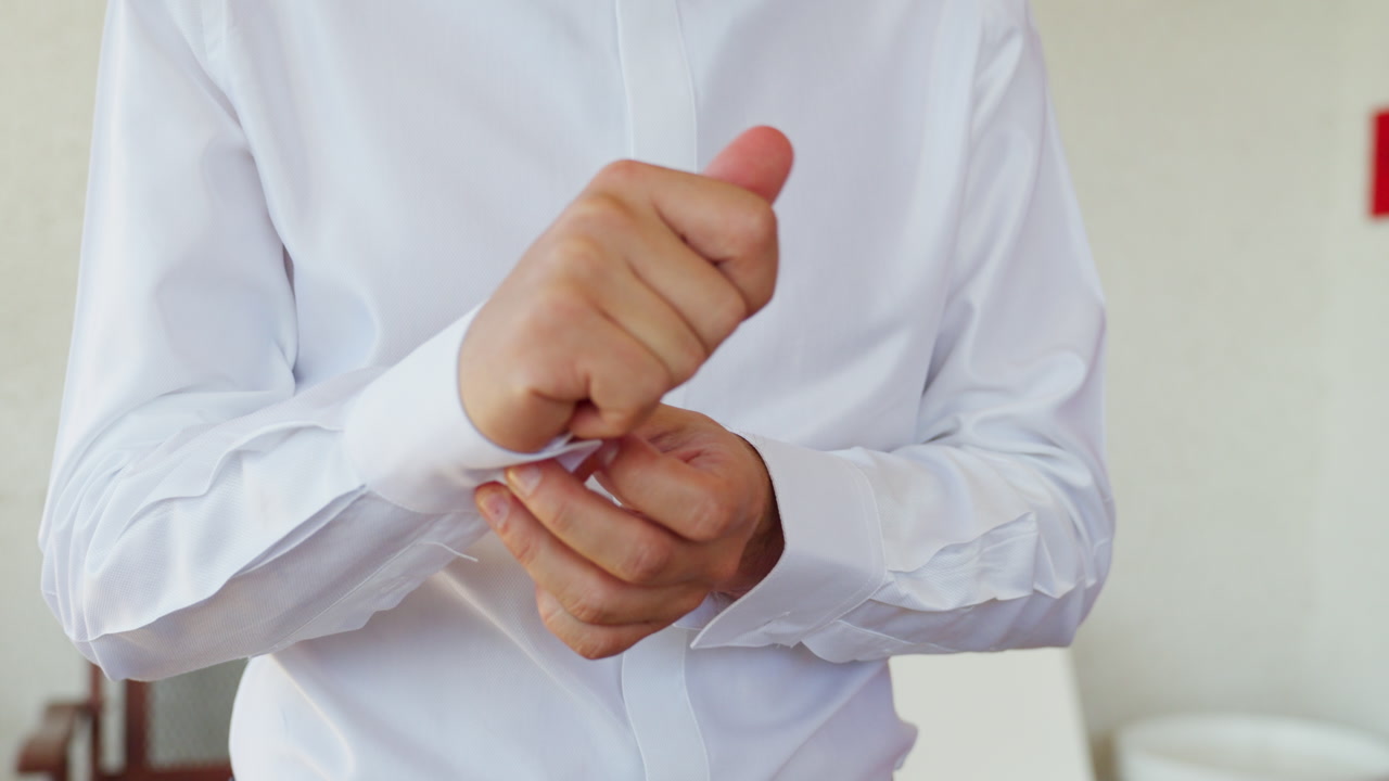Front view slowly moving closer to groom hands fastening cufflinks before ceremony.