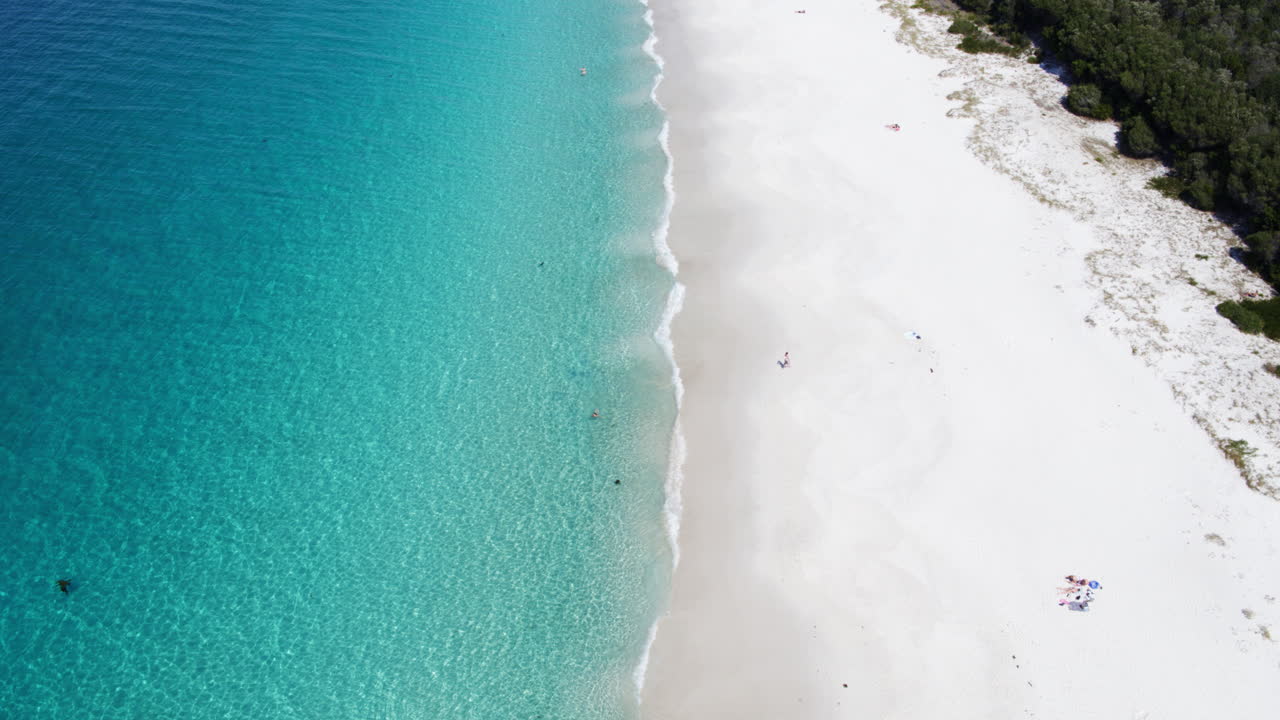 Aerial high angle pullback across tropical beach with clean surf and soft white sand