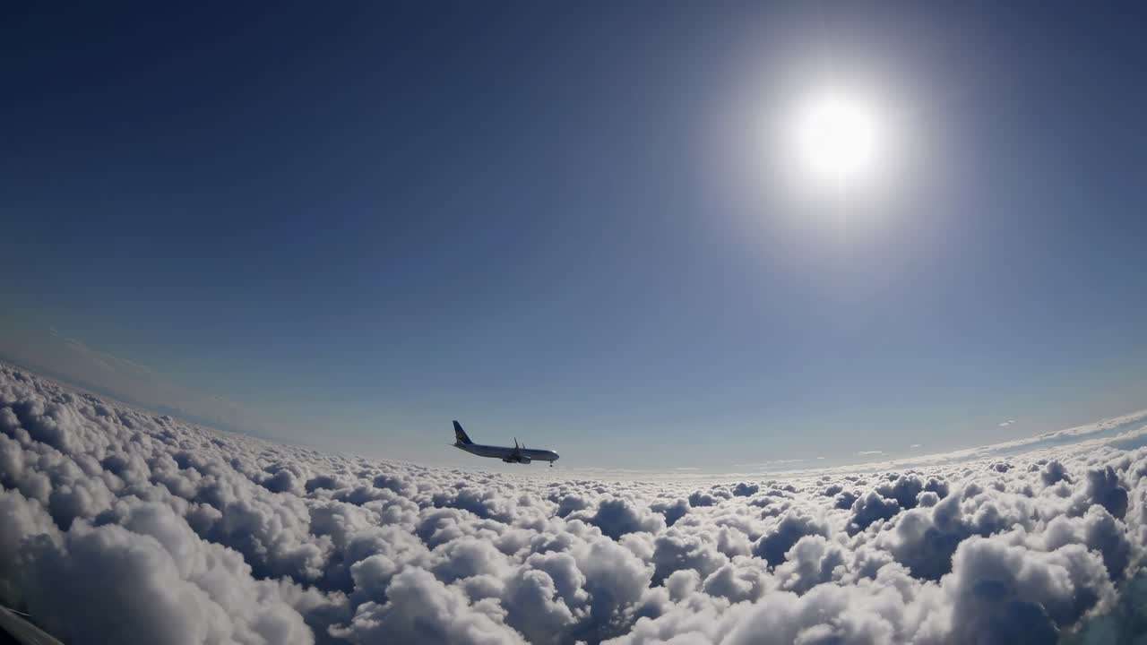 Un video aereo cattura un aereo che vola sopra nuvole soffici sotto un sole splendente, ripreso da un grandangolo