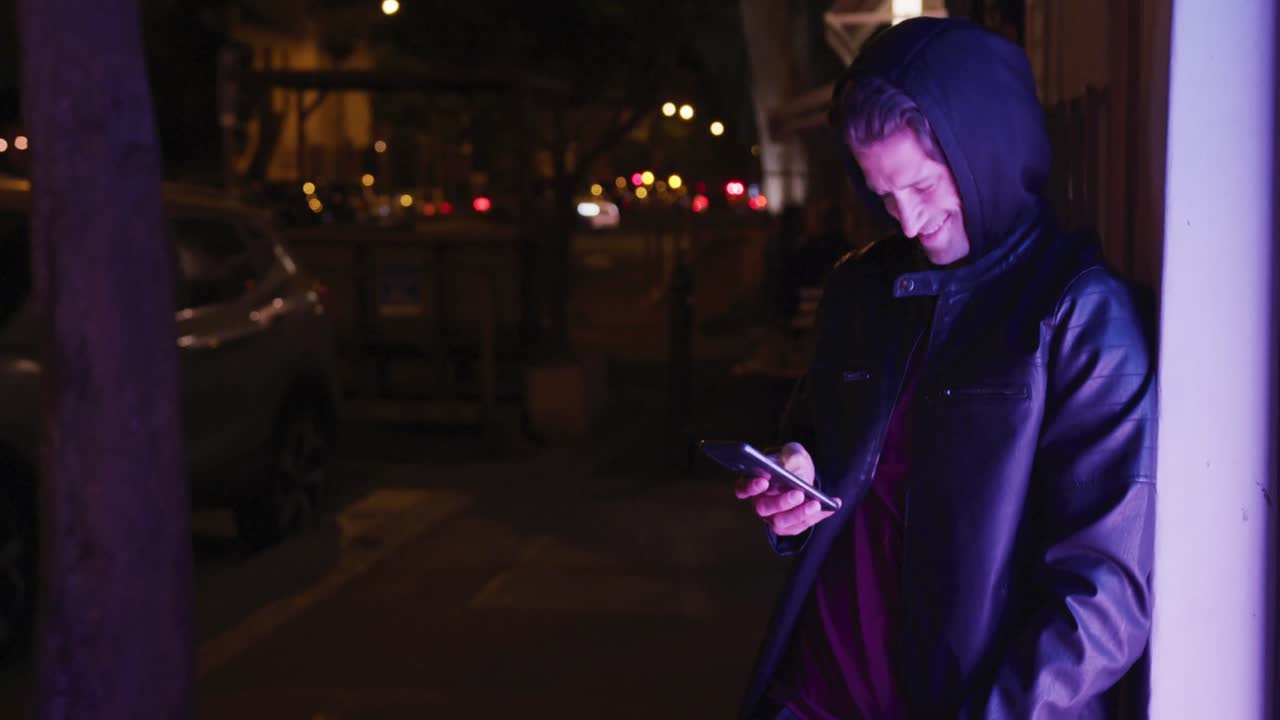 저녁에 벽에 누워서 웃고  ⁇ 드폰을 사용하는 백인 후드 남성