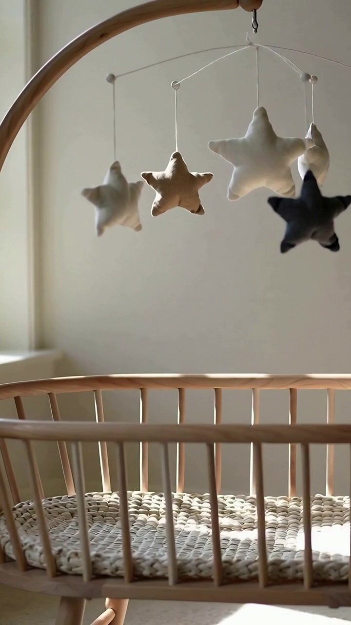 Video vertical: Móvil de estrellas meciéndose sobre una cuna de madera en casa, la brisa de la ventana izquierda moviendo la luz del sol.