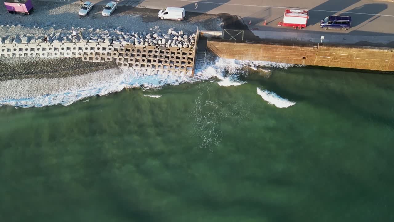 Aerial footage in slow motion over coastal Ireland with waves and surfers walking on the road